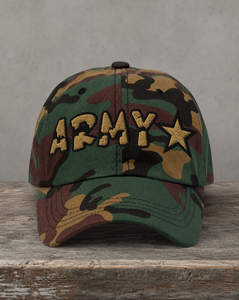 A camouflage baseball cap with 'ARMY' and a star embroidered in tan on the front, resting on a rustic wooden surface against a textured gray background.